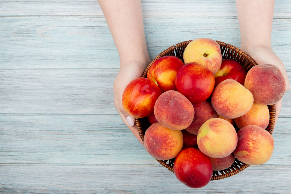 top-view-female-hands-holding-wicker-basket-with-fresh-ripe-nectarines-peaches-rustic-wood-with-copy-space