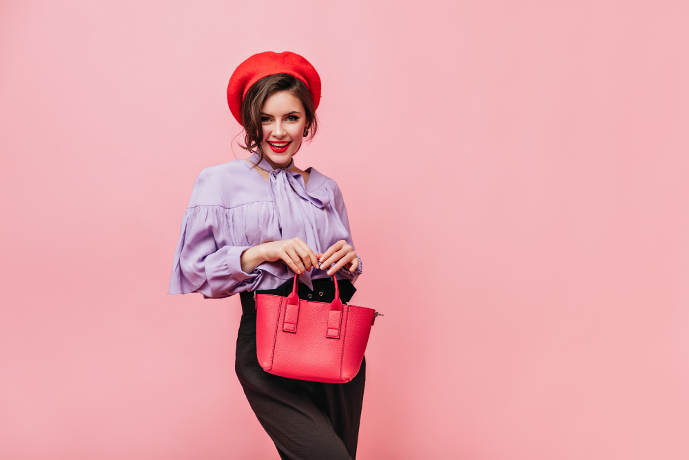flirtatious-woman-beret-blouse-trousers-holding-red-bag-pink-background